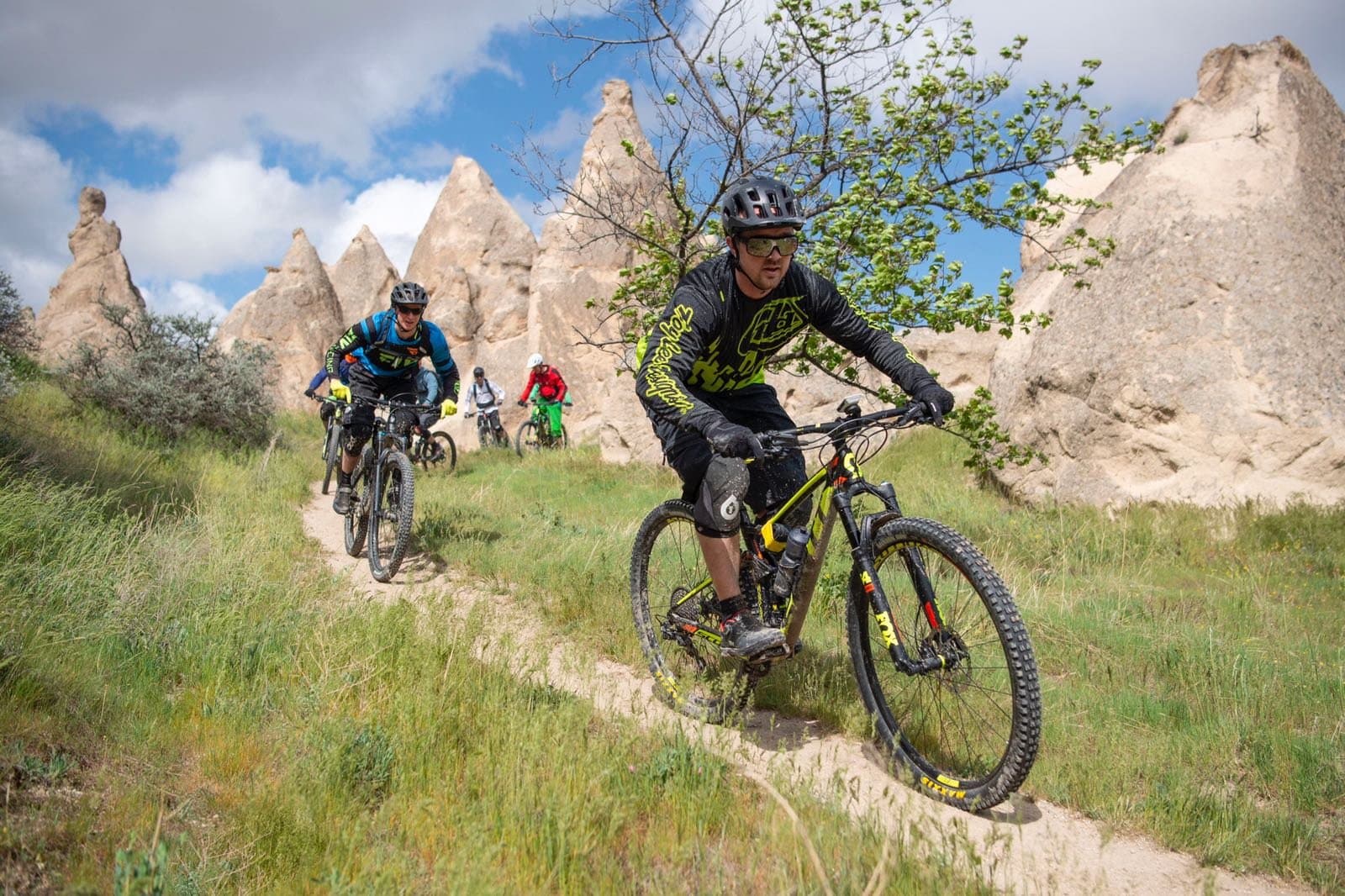 Mountain bikers riding past fairy chimney rock towers in a green Cappadocia valley