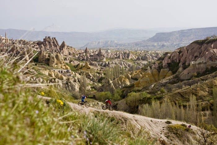 Two mountain bikers riding a trail through a hazy rock-studded valley in Cappadocia