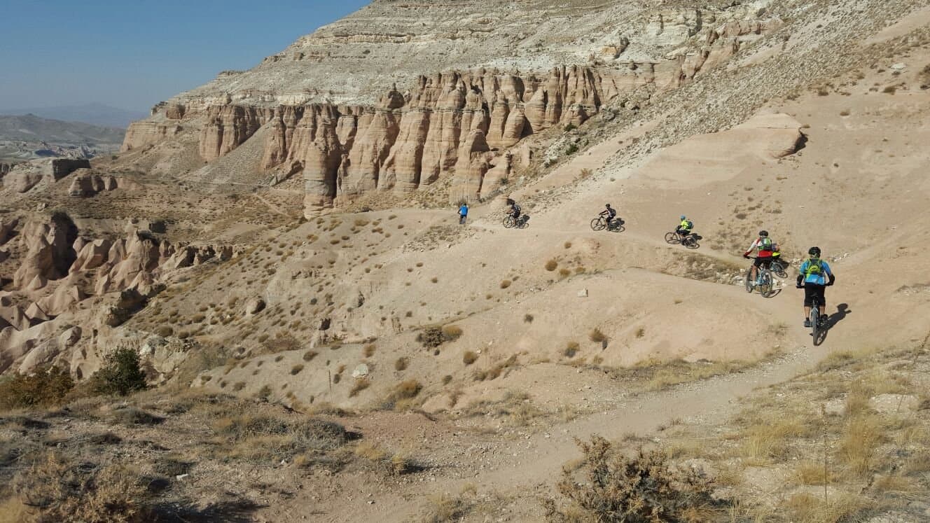Mountain bikers riding through a valley of pale rock formations in Cappadocia
