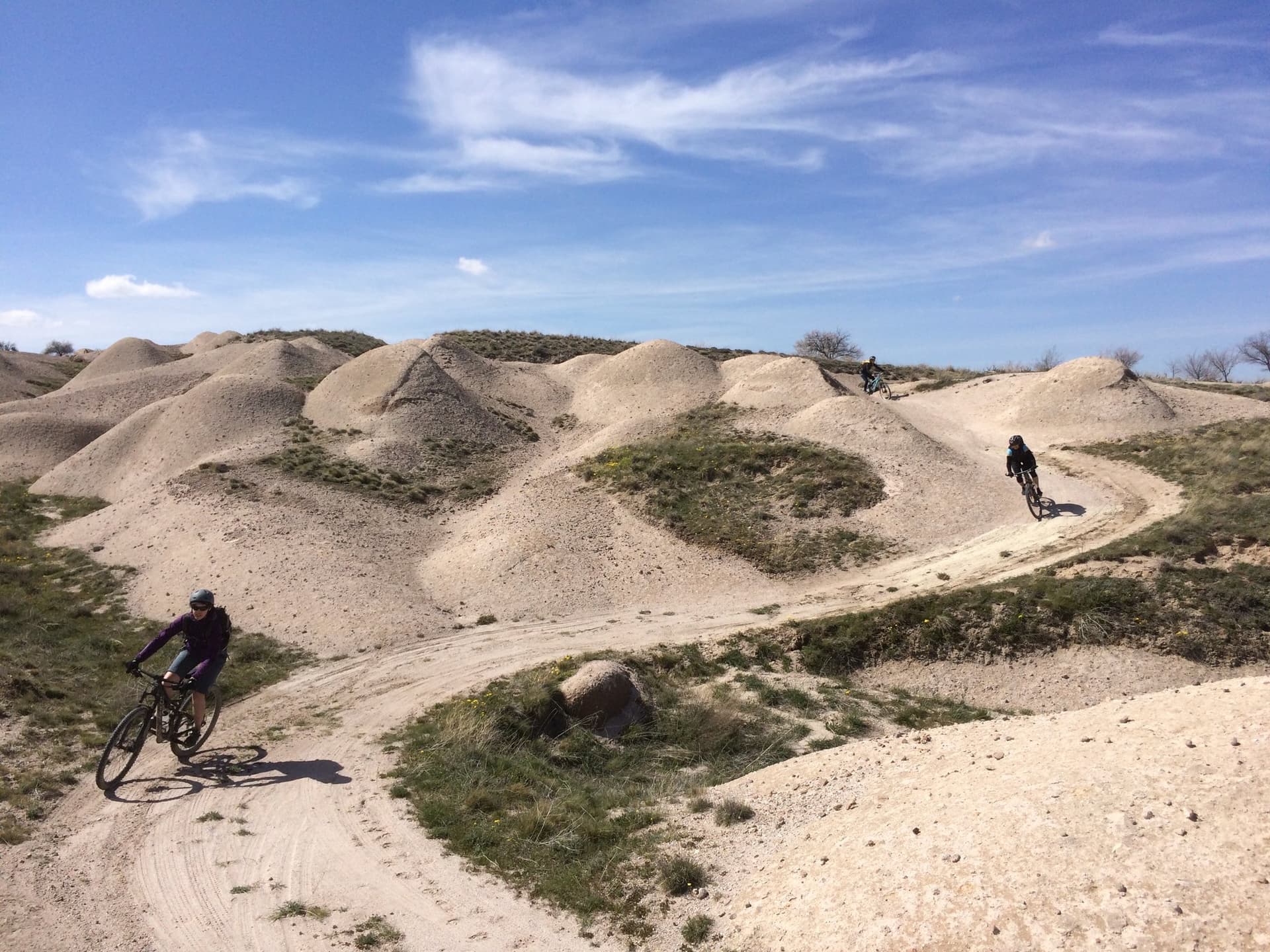 Mountain bikers riding a winding dirt track through pale sandy dune-like hills