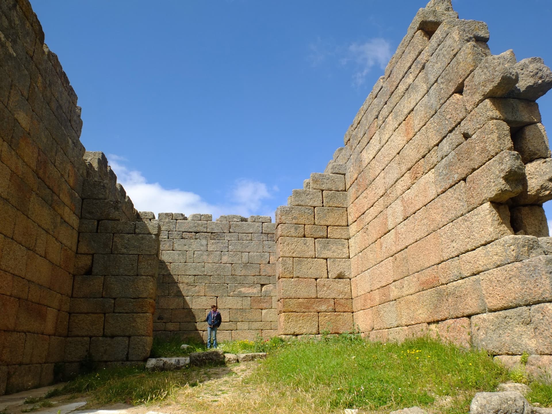 Person dwarfed by massive stone blocks of an ancient city wall