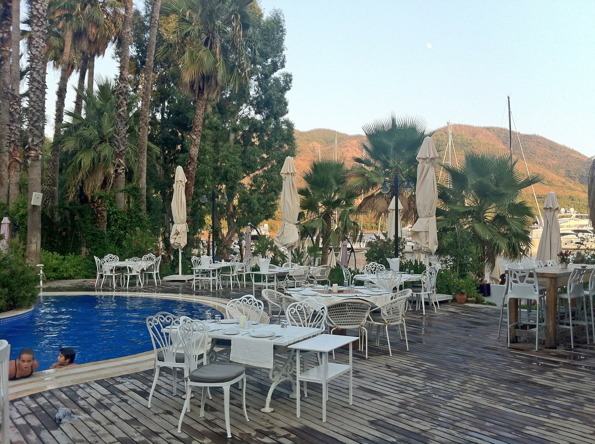 Poolside terrace with white lounge furniture and palm trees at a hotel on the Aegean coast