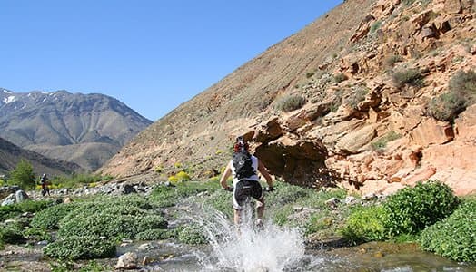 Rider splashing through a mountain stream beside a rocky outcrop in Morocco