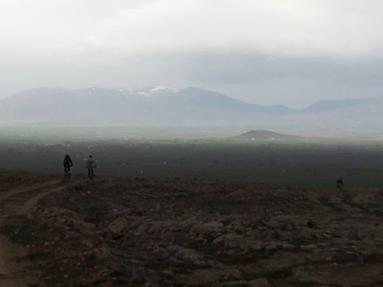 Riders crossing an open hazy plain with mountains in the distance