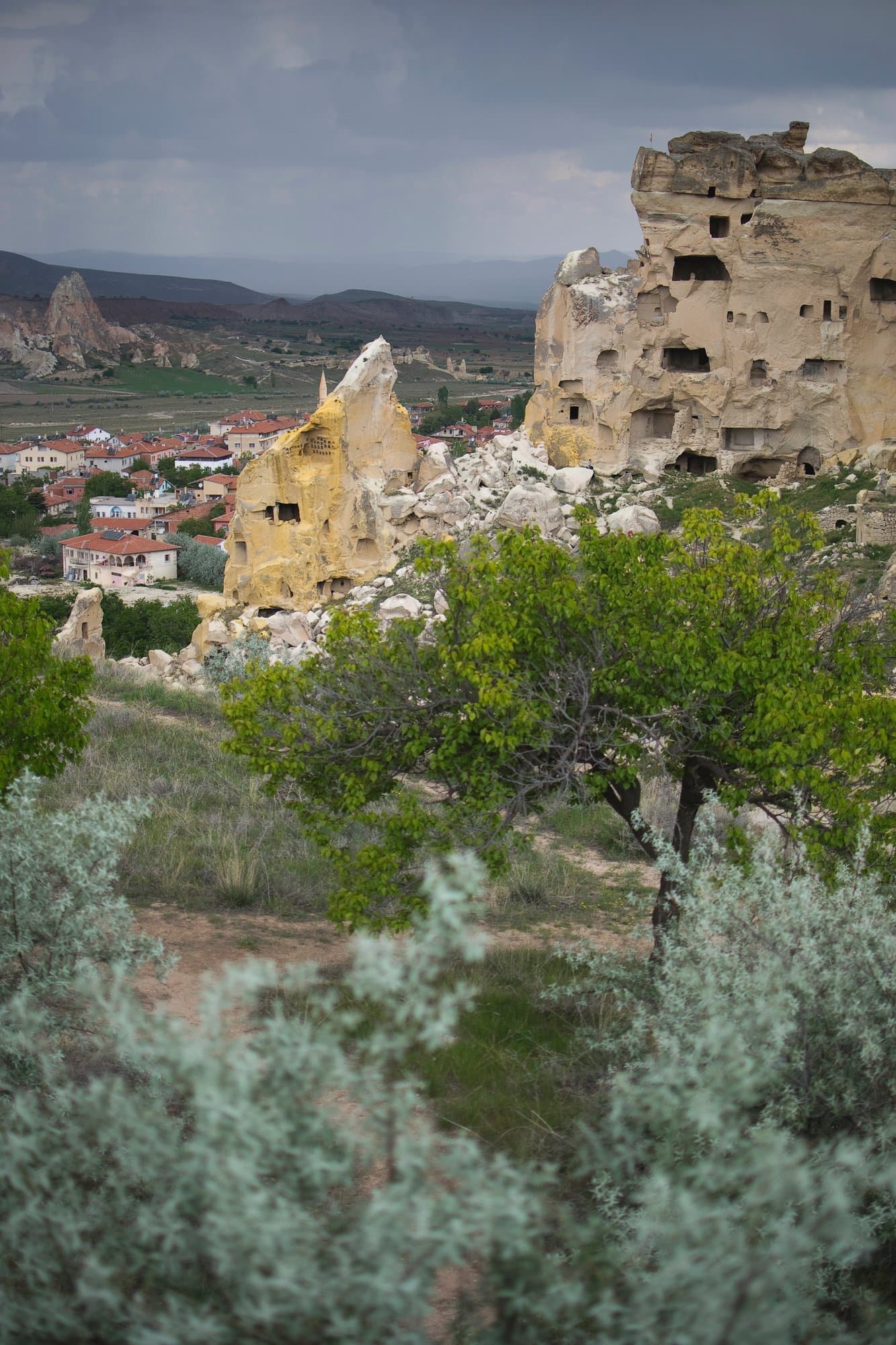 Rock-cut cave dwellings on a cliff above a green Cappadocia village