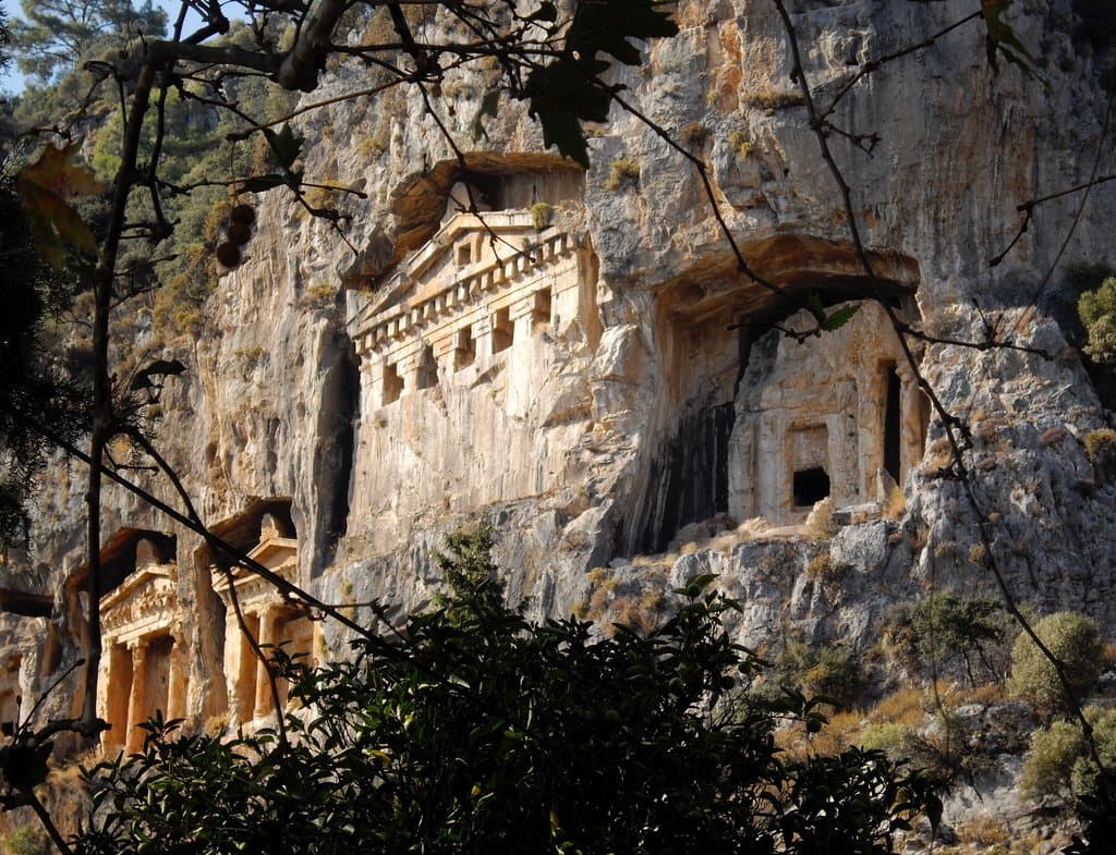 Rock-cut Lycian tombs carved into a cliff face above the coast