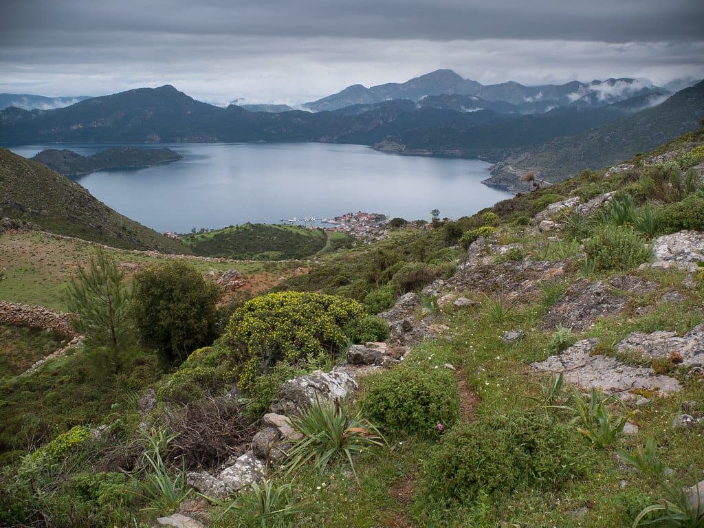 Rocky trail through scrub overlooking a bay and layered mountains