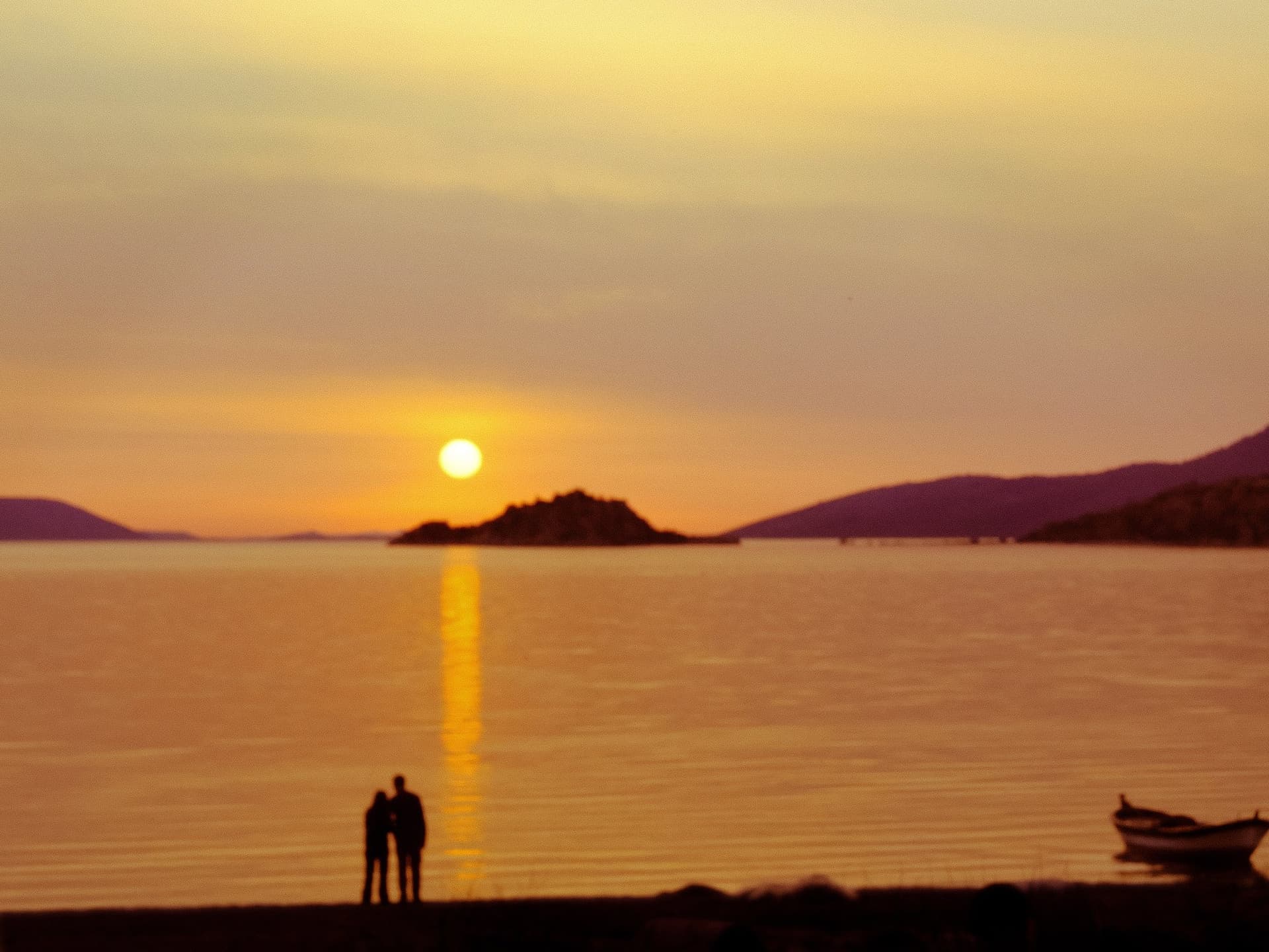 Silhouetted couple watching the sun set over the sea on the Aegean coast