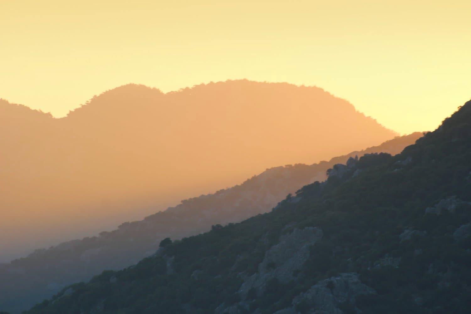 Silhouetted mountain ridges layered beneath a warm sunset sky