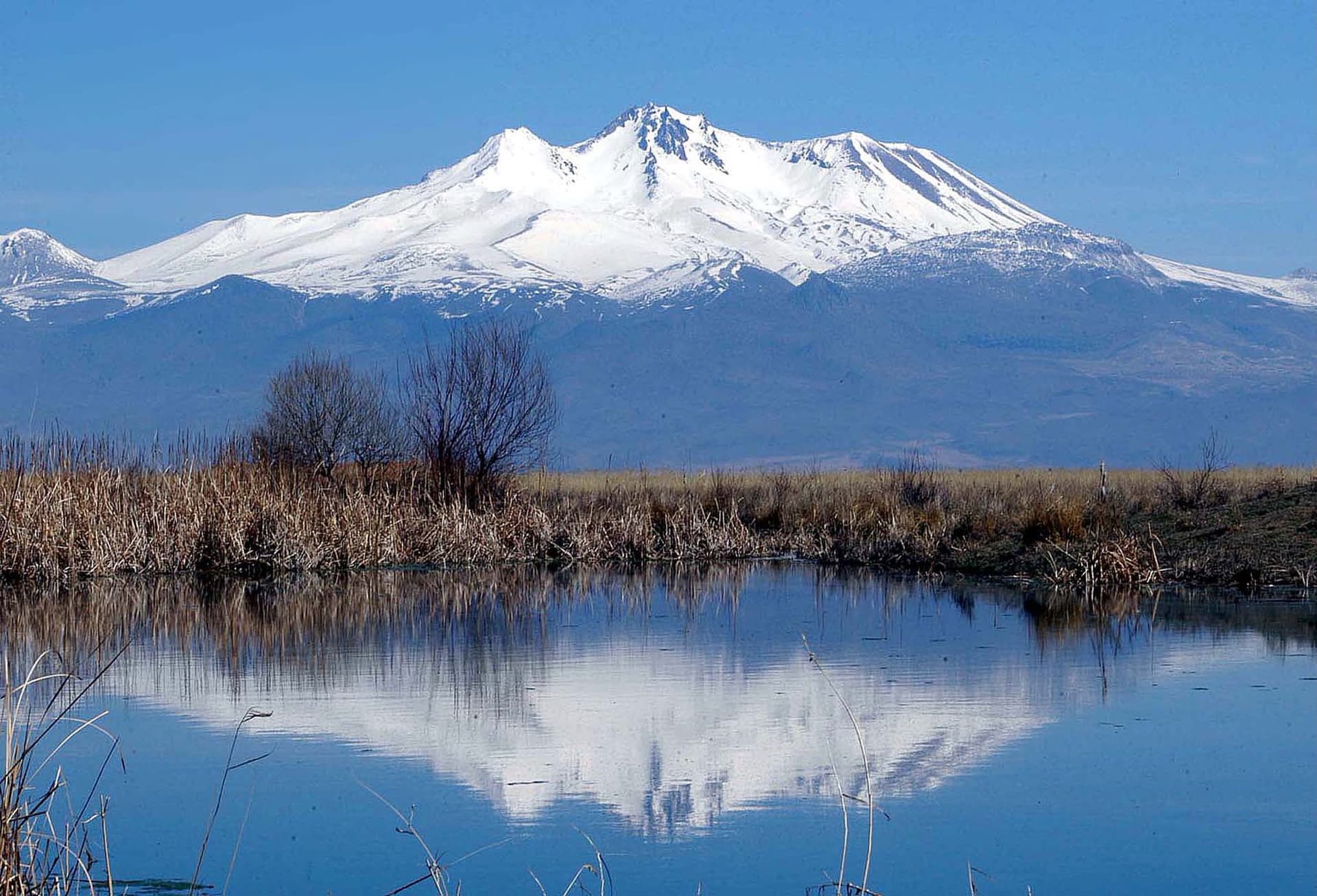 Snow-capped Mount Erciyes reflected in a still lake fringed with dry reeds