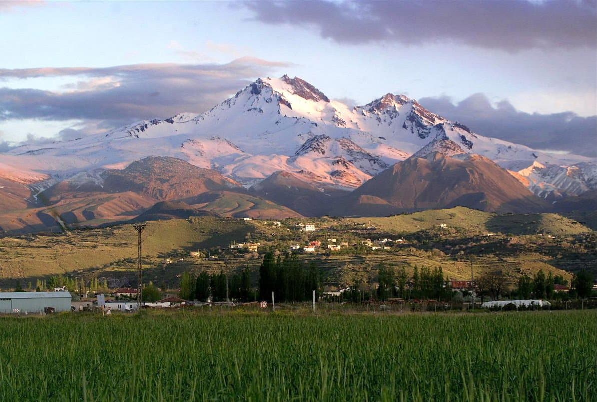 Snow-capped volcanic peak rising above green fields at sunrise in Cappadocia