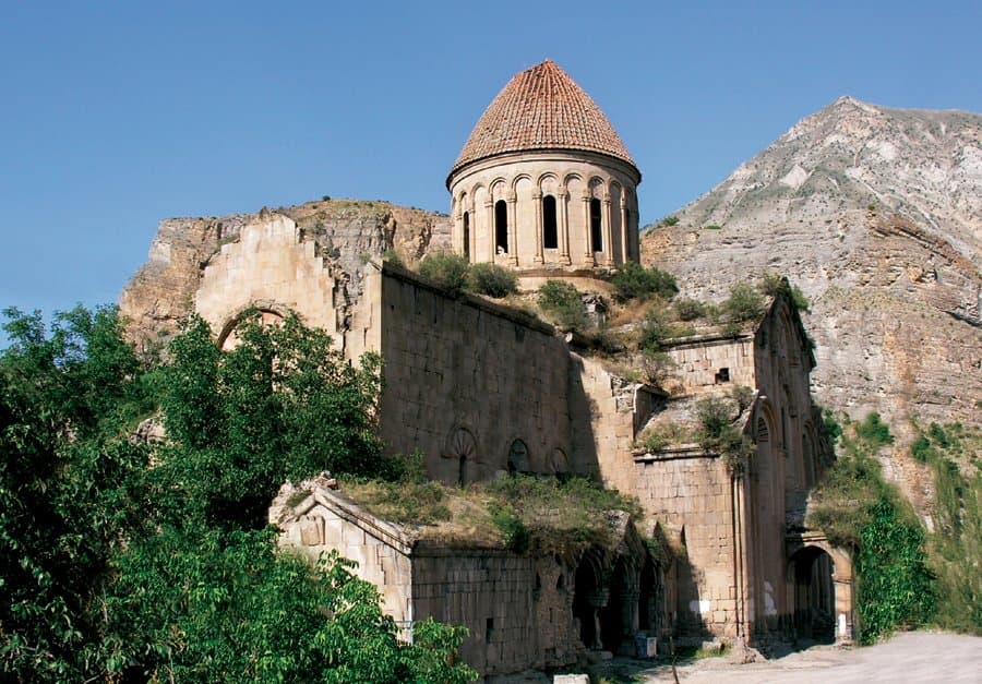 Stone Armenian church with a red conical roof set against the Kackar Mountains