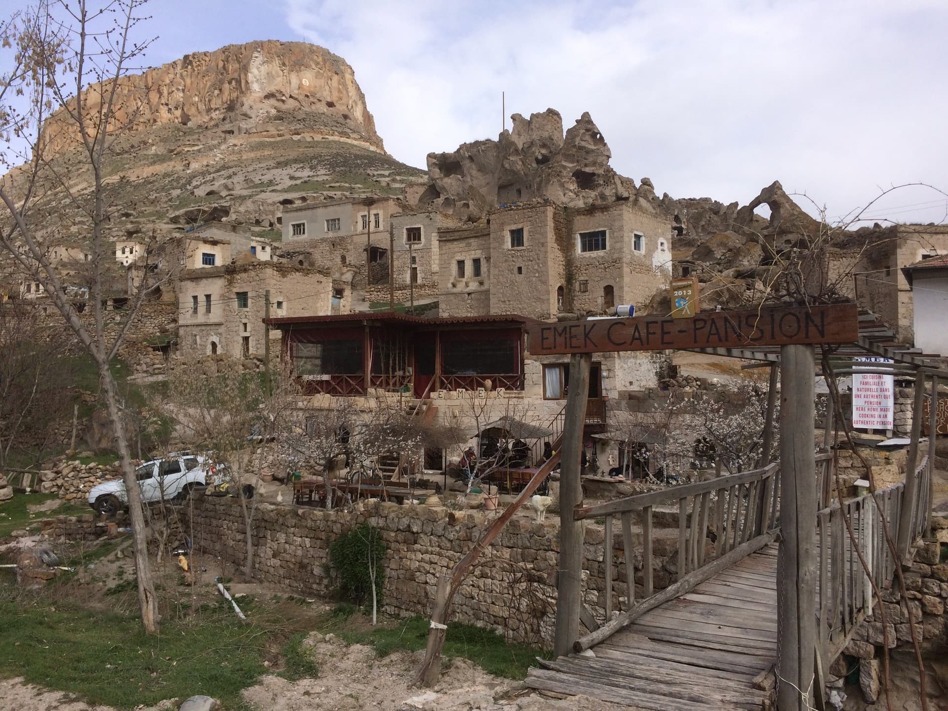 Stone village houses built into a cliff above a wooden footbridge in Cappadocia