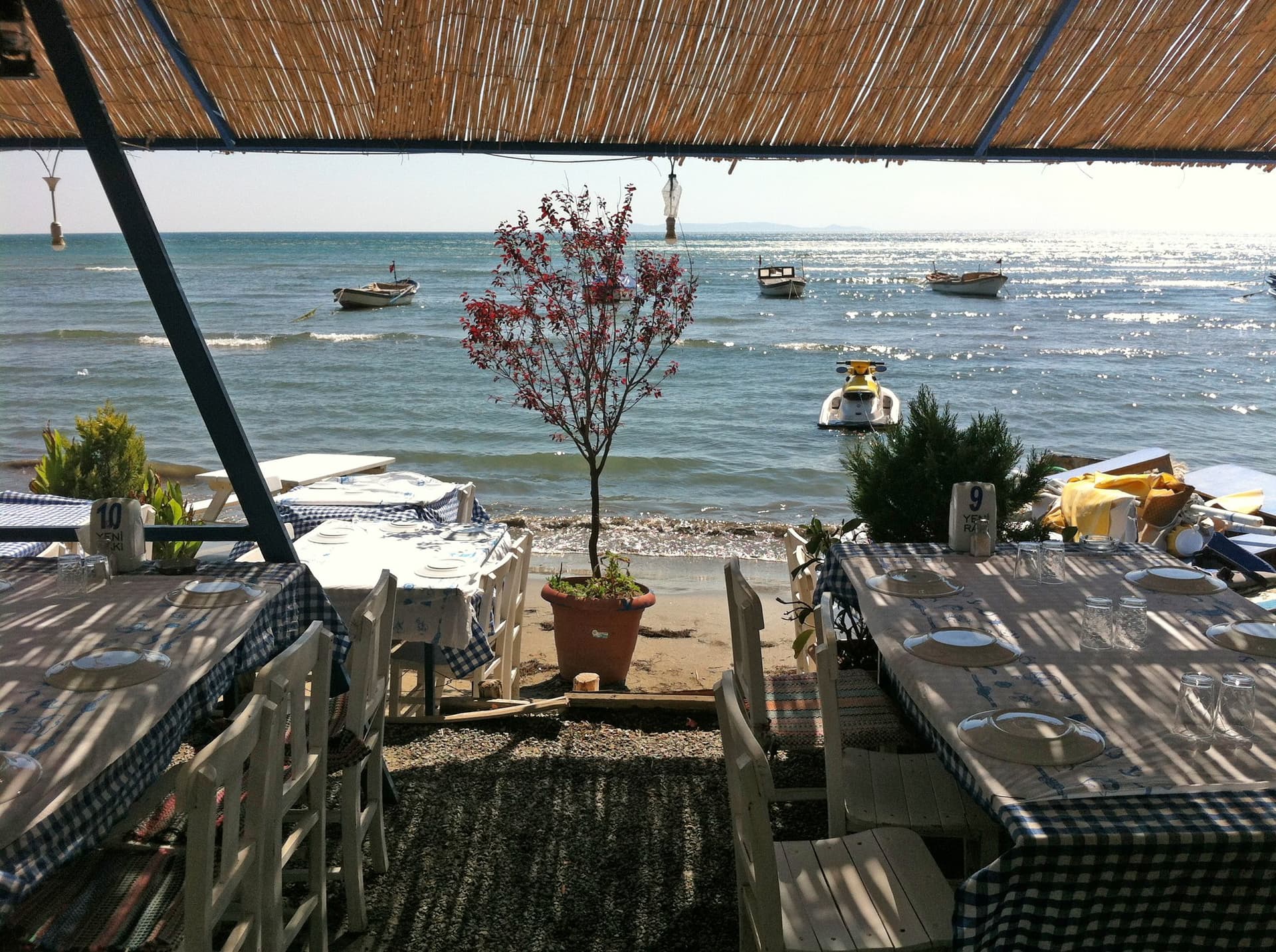 Tables set for dining under a thatched roof beside the Aegean shore
