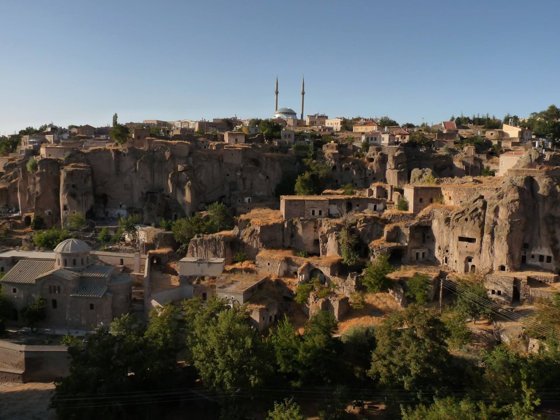 Town view with mosque minarets rising above cave dwellings and greenery