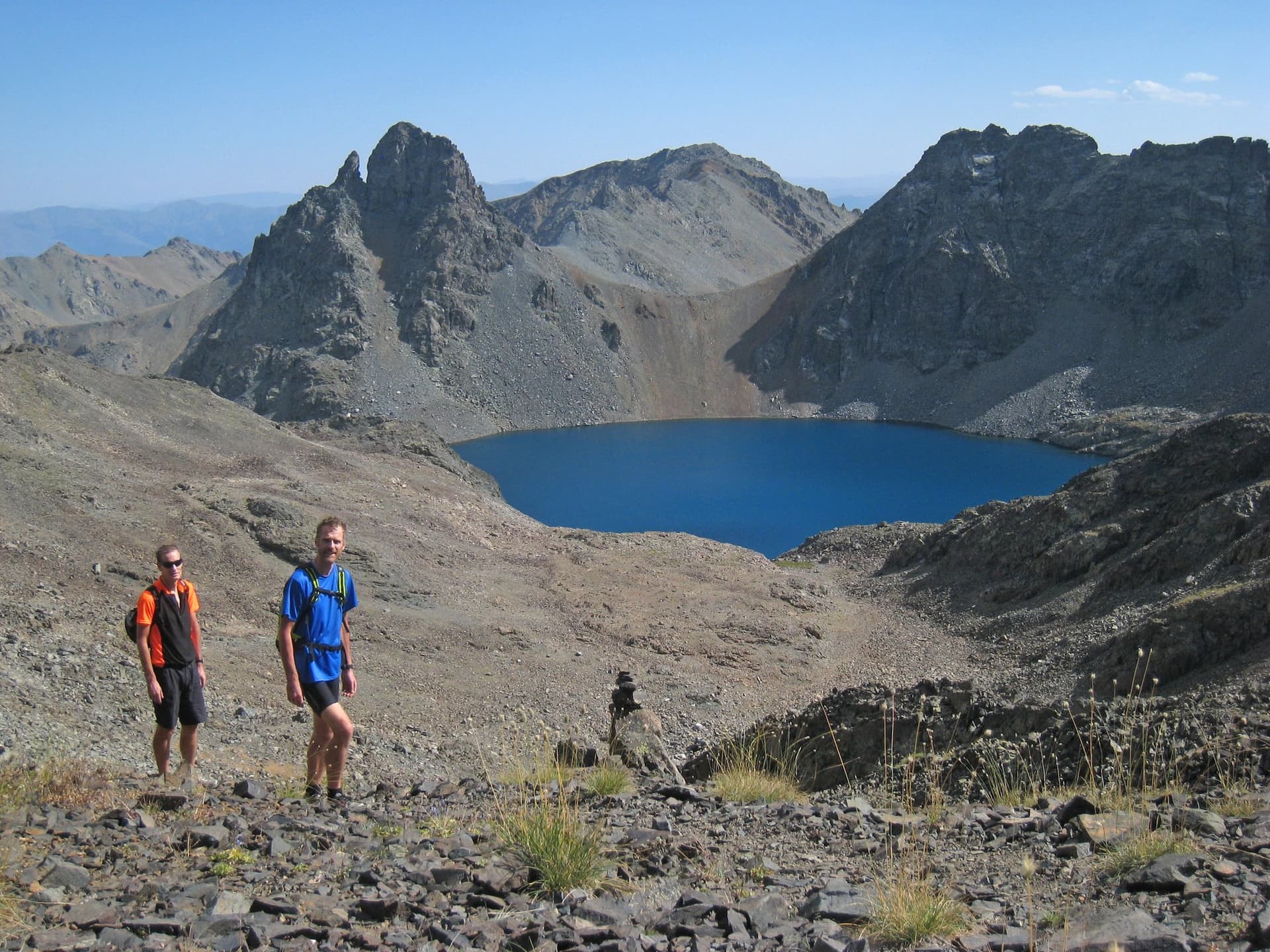 Walkers above a deep blue alpine lake ringed by the dark jagged peaks of the Kackar Mountains