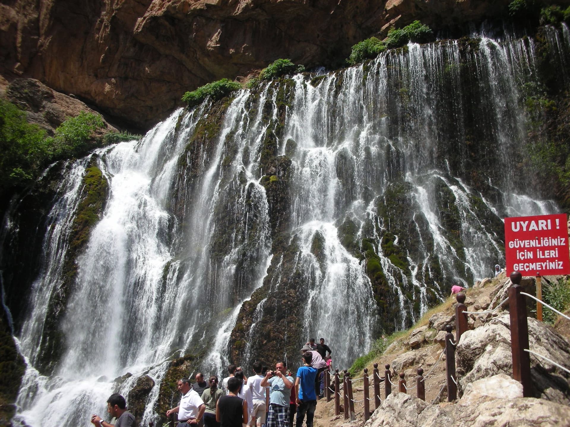 Waterfall cascading down a rock face as visitors watch from a marked trail
