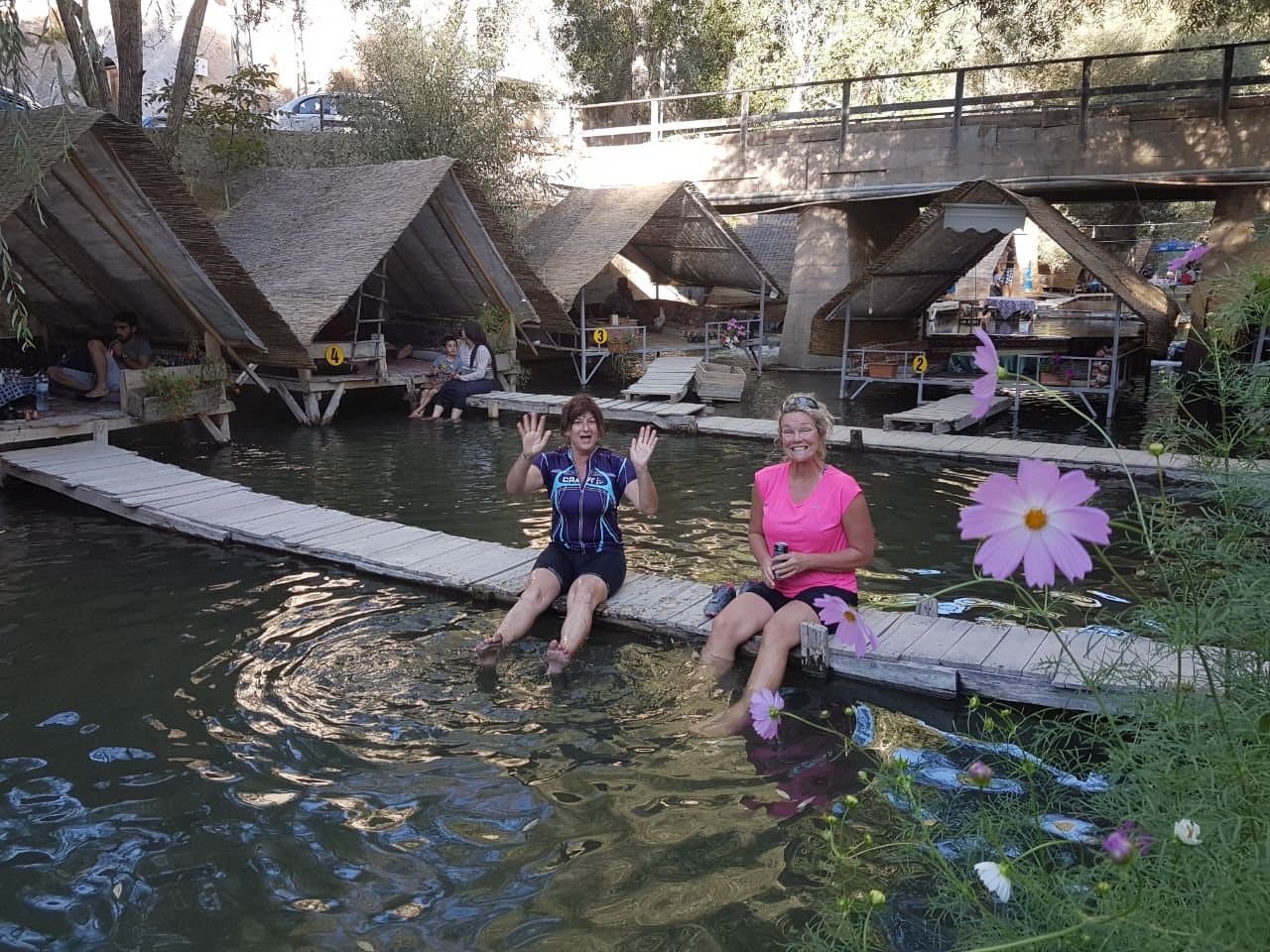 Two women sitting with their feet in a thermal pool surrounded by wooden huts